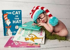 a baby wearing glasses and a knitted hat laying on top of books next to a cat in the hat