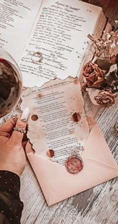 a person is writing on an old letter with a glass of wine in front of it