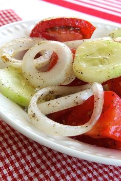 a white plate topped with cucumber onion and tomato salad next to a red checkered table cloth