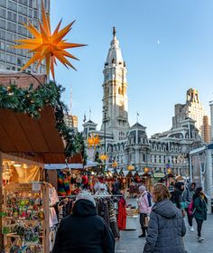 people are walking around an outdoor market with buildings in the background