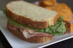 a sandwich with lettuce, ham and cheese on it next to potato chips