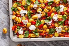 a tray filled with pasta and vegetables on top of a marble countertop next to other food items