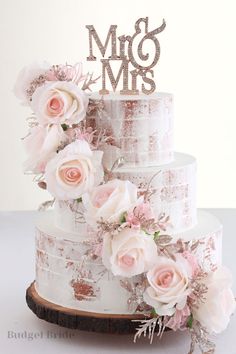 a wedding cake decorated with pink flowers and mr and mrs topper on a wooden slice