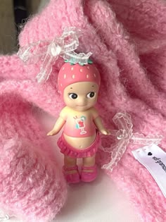 a small doll sitting on top of a pile of pink crocheted material next to a tag