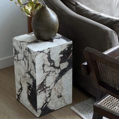 a black and white marble block with a vase on it next to a chair in a living room