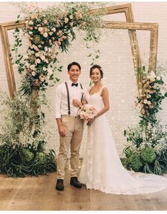 a man and woman standing in front of a floral arch