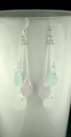 a pair of white and green glass earrings on a stand with a black surface in the background