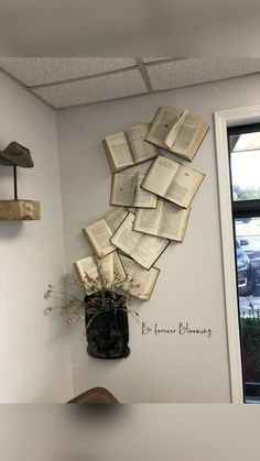 an arrangement of open books on the wall above a vase filled with flowers and plants