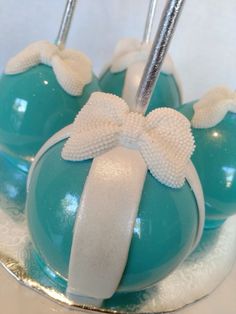 two blue cake pops with white bows on them sitting on top of a silver plate