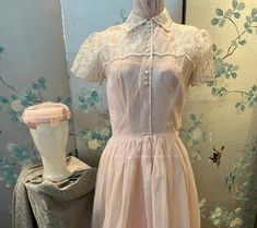 1950 vintage, pink organza dress with white embroidered leaves and flowers. The top has a high neck with a collar with 3 sets of white buttons, also in threes, down the front to the waist. The yoke over the shoulders, including the short sleeves, are embroidered.the hem of the full, gathered skirt is embroidered. The pink linen, circle hat is covered with pink netting decorated with pink leaves. The taffeta lining is strapless on the top. Bust 32", waist 26", bodice length 16", skirt length 33". 1950s Pink Vintage Wedding Dress, Pink Organza Dress, Circle Hat, Embroidered Leaves, 1950 Vintage, Organza Dress, Pink Leaves, Pink Hat, Pink Linen