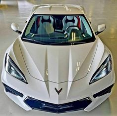 the front end of a white car in a showroom with other cars behind it