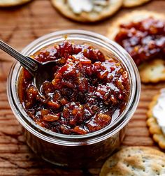 a jar filled with jam next to crackers on a wooden table and spoon in it