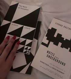 two black and white books on a bed with a person's hand holding one