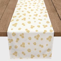 a white table runner with gold flowers on it and a wooden bench in the background