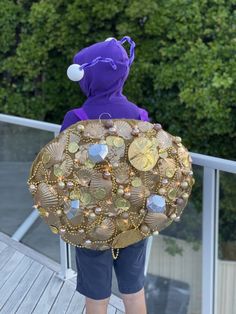 a person wearing a purple hoodie and blue shorts holding a large gold purse on top of a wooden deck