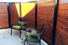 two chairs sitting next to each other in front of a wooden fence with green cushions