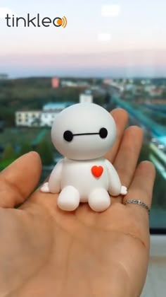 a hand holding a small white toy with a red heart on it's chest