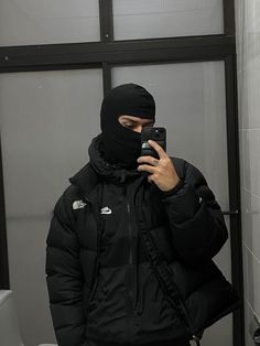 a man in a black jacket taking a selfie while wearing a mask and holding a cell phone