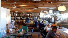 people sitting at tables in a restaurant with lots of lights hanging from the ceiling above them