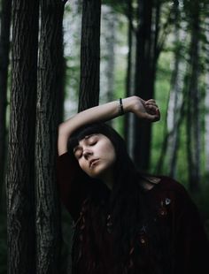 a woman is standing in the woods with her hands on her head and eyes closed