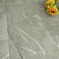 a vase filled with yellow flowers sitting on top of a stone floor covered in cracks