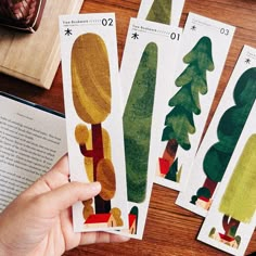 someone is holding four different trees in front of an open book on a table with other books