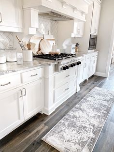 a kitchen with white cabinets and marble counter tops, an area rug and flowers on the floor