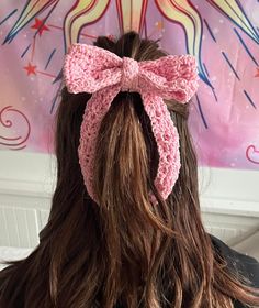 a woman with long hair wearing a pink crochet bow in front of a painting