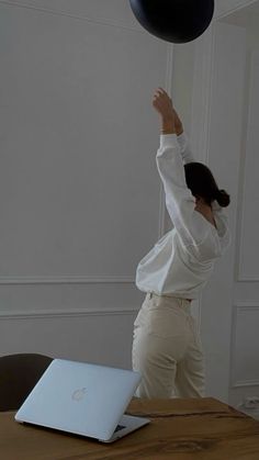 a woman in white shirt throwing a black ball over her head at a laptop computer