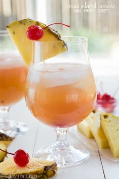 two glasses filled with pineapple punch on top of a white table next to sliced pineapples