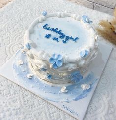 a white cake with blue frosting and butterflies on it sitting on a table next to a teddy bear