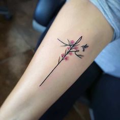 a woman's arm with a small branch and flowers tattoo on the left forearm