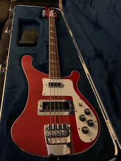 a red and white bass guitar sitting in a case on top of a blue cloth