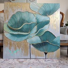 a painting with blue leaves on it in front of a couch and coffee table next to a chair