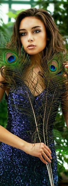 a woman in a blue dress holding two peacock feathers