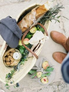 a person is holding a basket full of food and other items on the ground next to them