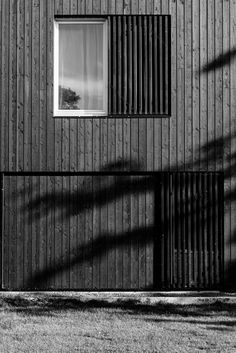 a black and white photo of a building with a window on the side, next to a tree