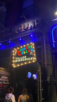 people are standing in front of a neon sign that says comedy cellar, village underground