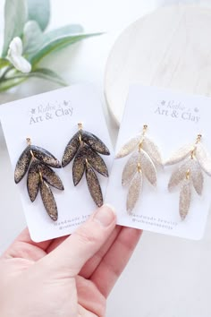 two pairs of gold and silver leaf earrings on top of a white card next to a plant