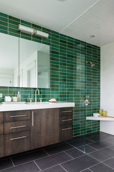 a bathroom with green tiles and wooden cabinets in the corner, along with a large mirror on the wall