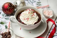 a white plate topped with a cup filled with whipped cream and chocolate chips next to christmas decorations