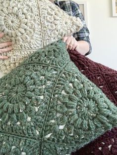 a woman holding two crocheted blankets in her hands