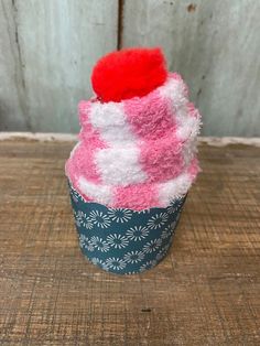 a pink and white cupcake with a red pom - pom on top