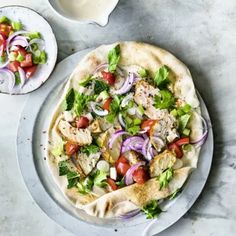 a pita with chicken, lettuce and tomatoes on it next to a bowl of dressing