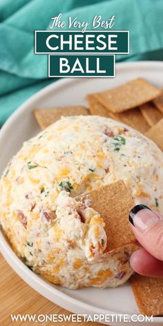 a hand holding a cracker over a cheese ball on a plate with crackers