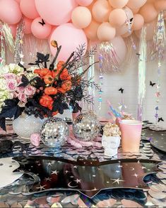 a table topped with balloons and confetti next to a vase filled with flowers