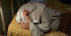 an older man laying on top of a bed covered in a blanket and covering his face