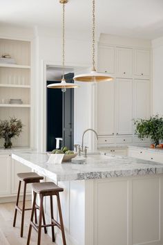 a large kitchen with white cabinets and marble counter tops, along with two stools in front of the island