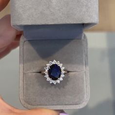 a woman's hand holding an engagement ring with a blue stone surrounded by white diamonds