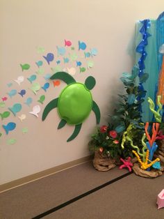 there is a green turtle on the wall next to some plants and other decorations in front of it